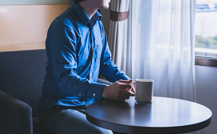 コーヒーを飲みながら外を眺める男性